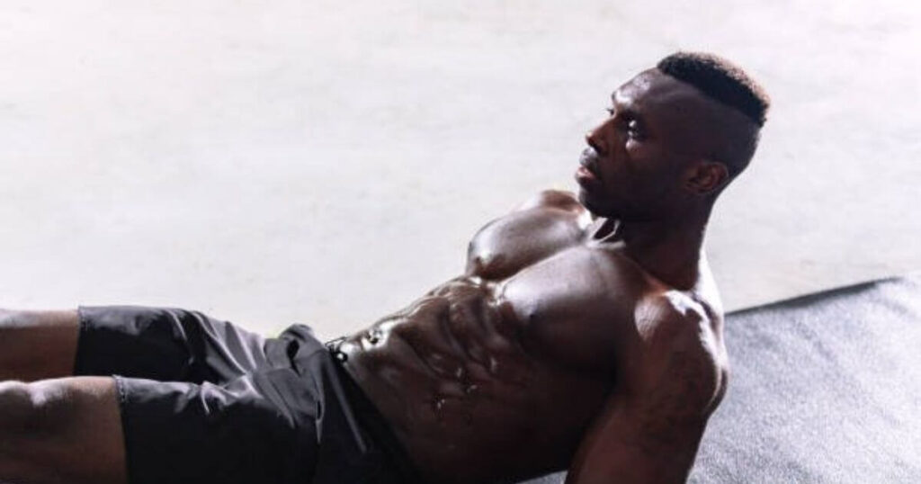 A muscular man is performing an abdominal exercise on a mat, lying on his back with his upper body slightly elevated.