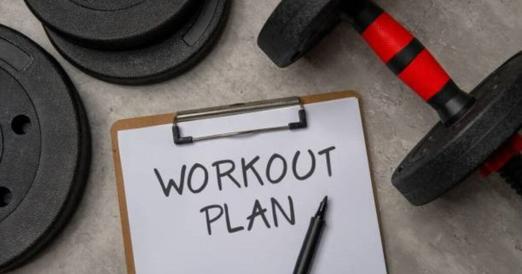 A clipboard with the words "WORKOUT PLAN" written on it, placed next to dumbbells on a gym floor.