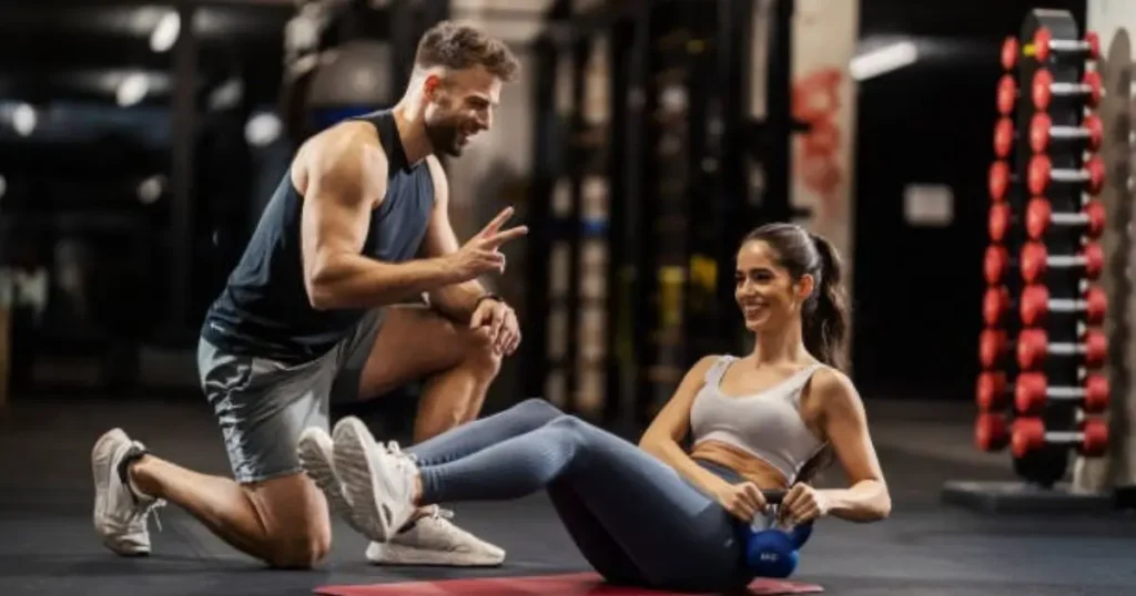 "A man and a woman in a gym, with the woman performing an exercise on a mat while the man encourages her."