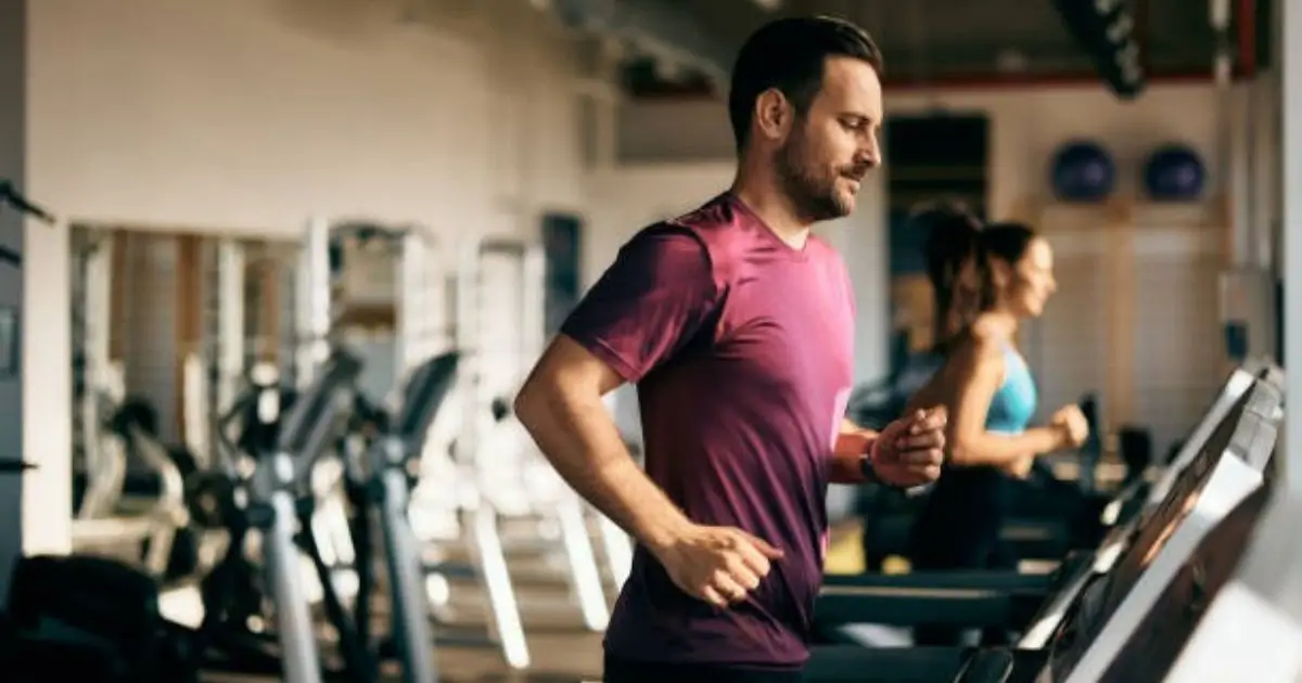 "A man running on a treadmill in a gym, with others exercising in the background."