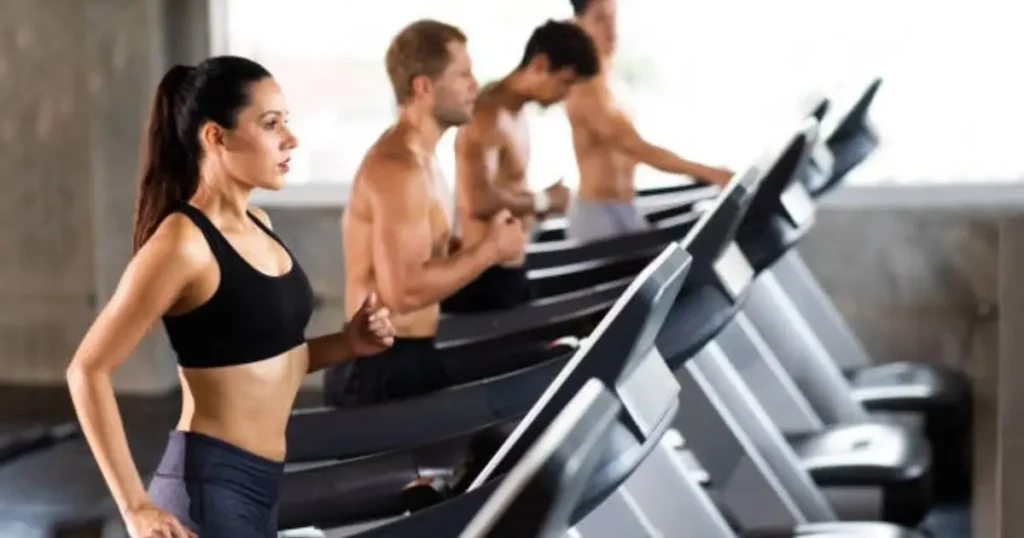 A group of individuals is exercising on treadmills in a modern gym, with one woman leading the lineup.