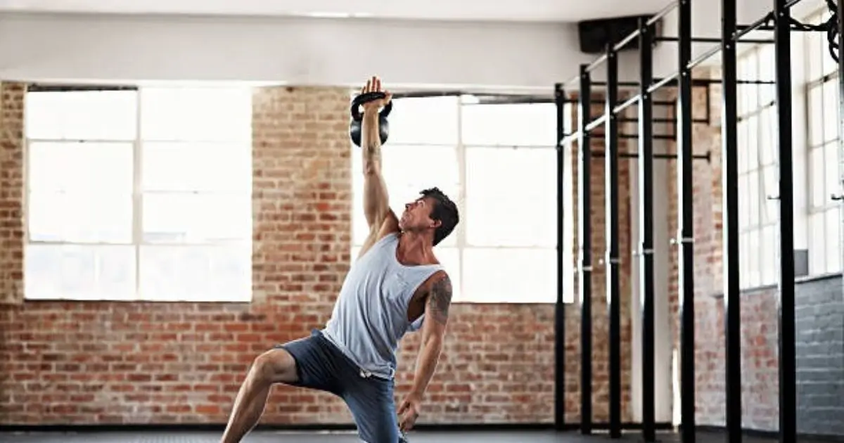 A man is performing a kettlebell swing in a gym with exposed brick walls and large windows, showcasing his strength and form.